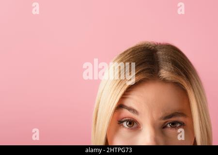 vista ritagliata della donna bionda accigliata isolato su rosa, immagine stock Foto Stock