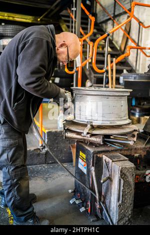 Officina del garage per pneumatici. Il personale del garage pulisce un cerchione con una spazzola metallica pneumatica prima di montare lo pneumatico. Foto Stock