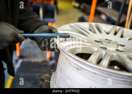 Officina del garage per pneumatici. Il personale del garage pulisce un cerchione con una spazzola metallica pneumatica prima di montare lo pneumatico. Foto Stock
