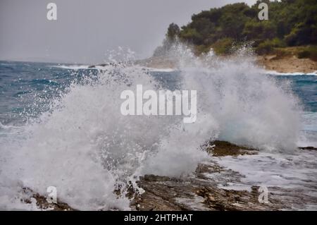 Grande onda spruzzi nella spiaggia rocciosa croata durante il vento forte sul Mare Adriatico. Linea orizzonte. Foto Stock