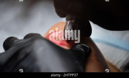 Cosmetologo in guanti neri makeup permanente sulle labbra della donna con tatuaggio penna macchina. Processo di microblading Foto Stock