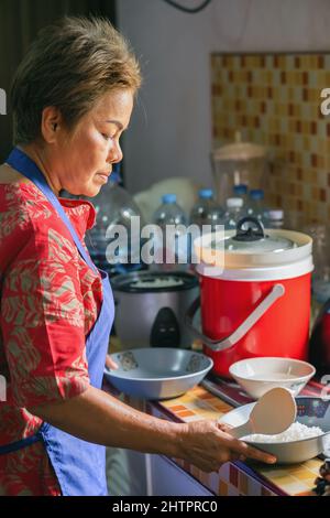 Thai bella donna che cucina riso per la famiglia in cucina. Persone reali Foto Stock