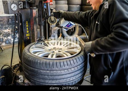 Officina del garage per pneumatici. Il personale del garage ha montato un pneumatico nuovo su un cerchio in lega utilizzando una macchina smontagomme per auto Foto Stock