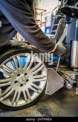 Officina del garage per pneumatici. Il personale del garage rimuove uno pneumatico su un cerchio in lega utilizzando una macchina per la sostituzione di pneumatici per auto. Foto Stock