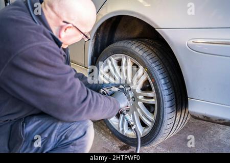 Officina del garage per pneumatici. Il personale del garage può rimontare una ruota su un'auto utilizzando una chiave pneumatica. Foto Stock