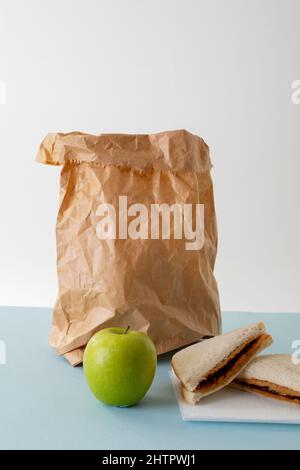 Mela verde con sacchetto di carta e burro di arachidi e sandwich gelatina sul tavolo su sfondo grigio Foto Stock