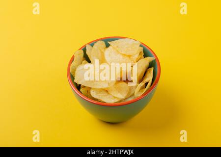 Primo piano ad angolo elevato delle patatine in un recipiente verde su sfondo giallo Foto Stock