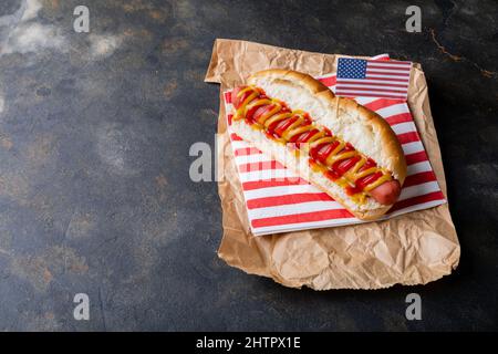 Bandiera americana su hot dog con salsa di pomodoro e mostered su carta di cera marrone a tavola Foto Stock