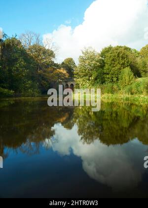 Vista ricca, saturata e illuminata dal sole del Viadotto di Hampstead con la struttura, gli alberi e il cielo blu profondo riflesso nelle acque del lago. Foto Stock
