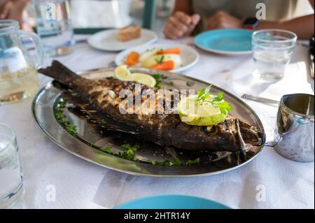 Pesce cernia alla griglia su un piatto d'argento in un ristorante a Creta, Grecia. Pesce al forno decorato fine servito in un ristorante di pesce a Creta, Grecia è serv Foto Stock