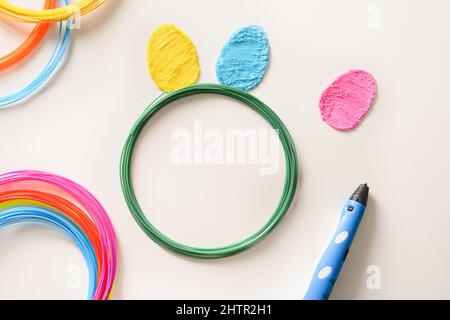 Uova colorate creative e orecchie conigliere per la festa di Pasqua di filamenti di plastica 3D penna su sfondo bianco. Giocattolo per bambini. Vista dall'alto. Foto Stock