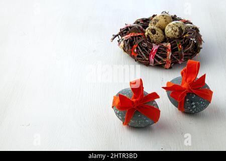 Uova di pollo dipinte legate con un nastro rosso sullo sfondo di un nido d'uccello su un tavolo di legno bianco. Sfondo carta di Pasqua Foto Stock