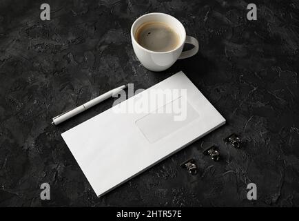 Foto della busta vuota, della tazza da caffè, della penna e delle clip su sfondo di pietra nera. Marcare a caldo su. Foto Stock