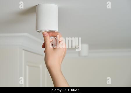 Una donna cambia una lampadina a risparmio energetico a soffitto con lampada a LED in un salotto di casa. Lavori in altezza, fai da te Foto Stock