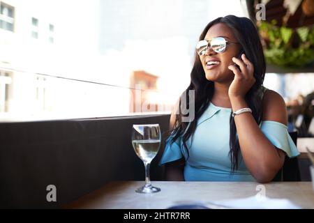 Im al ristorante. Scatto di una ragazza allegra che parla al telefono mentre si gusta un bicchiere di vino in un ristorante durante il giorno. Foto Stock