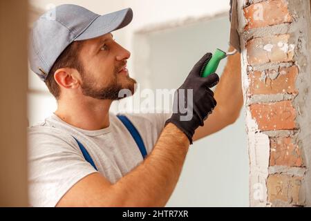 Ritratto di un uomo sorridente o di un artigiano che riempie il muro, preparandolo per la pittura Foto Stock