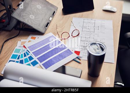 Primo piano di occhiali, progetto architettonico con carte e campioni di colore, thermos matraccio su scrivania creativa Foto Stock