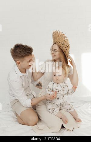 Ritratto di giovane famiglia sorridente felice in vestiti bianchi con il piccolo grumo impressionante blu-occhio bambino bambino bambino seduta. Foto Stock