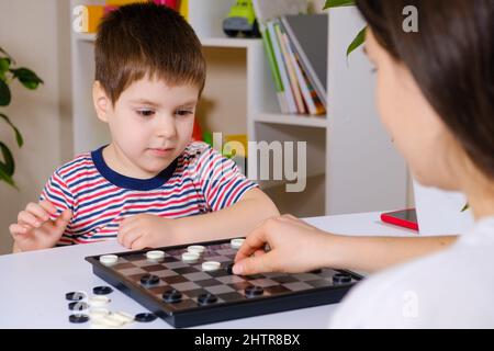 Madre e figlio giocano a dama in casa. Giochi da tavolo per bambini e bambini Foto Stock