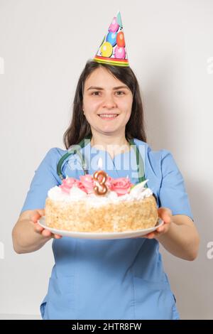 Il medico o l'infermiere tiene una torta di compleanno con il numero tre per l'anniversario dell'apertura della clinica Foto Stock