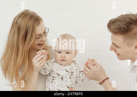 Ritratto di giovane felice sorridente bella famiglia con cherubico occhio blu bambino bambino toddler in vestiti bianchi seduti. Foto Stock