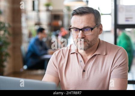 Uomo d'affari maturo in occhiali concentrandosi sul suo lavoro sul laptop che lavora in ufficio Foto Stock