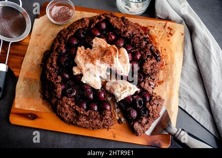 Galette di cioccolato al bourbon Cherry a fette con panna montata: Rustica galette di ciliegia al cioccolato fondente della foresta nera con panna montata impolverata Foto Stock
