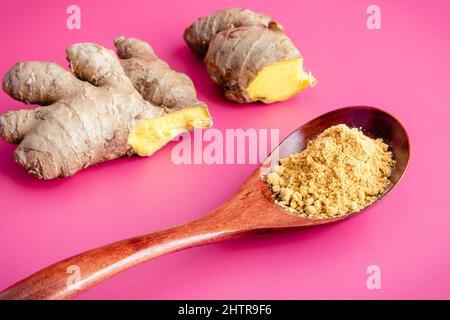 Zenzero macinato con radice di zenzero fresco: Un cucchiaio di zenzero macinato con zenzero crudo sullo sfondo Foto Stock