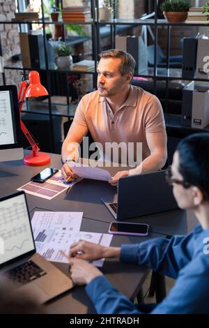 Gli uomini d'affari seduti al tavolo e che lavorano con documenti finanziari, analizzano e costruisce la strategia durante la riunione in ufficio Foto Stock