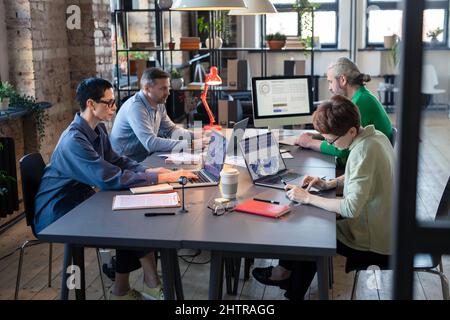Gruppo di uomini d'affari seduti al tavolo e che lavorano con grafici sui computer durante il lavoro di squadra nella sala riunioni Foto Stock