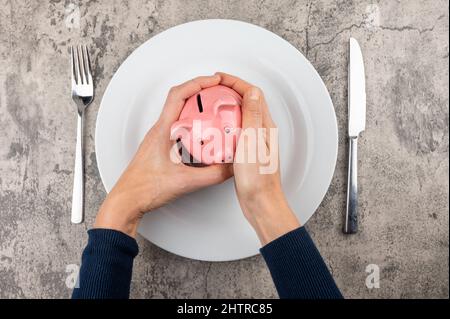Foto delle mani dell'uomo che tengono una fascia di piggy sopra un piatto vuoto - concetto di consapevolezza Foto Stock