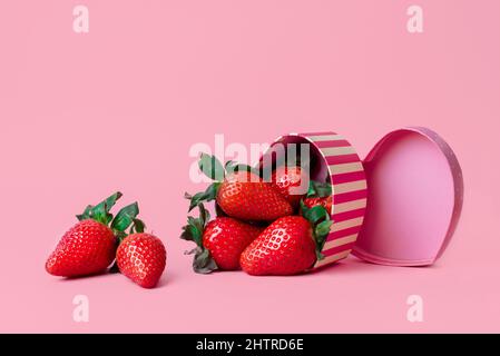 Piccola scatola a forma di cuore piena di fragole fresche su sfondo rosa Foto Stock