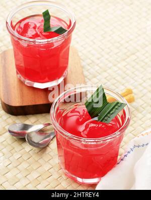 Manisan Kolang-Kaling (frutti di palma di zucchero conservati) di colore rosso. Servito in un bicchiere con Coaster di legno e foglie di Pandan come guarnitura. Foto Stock