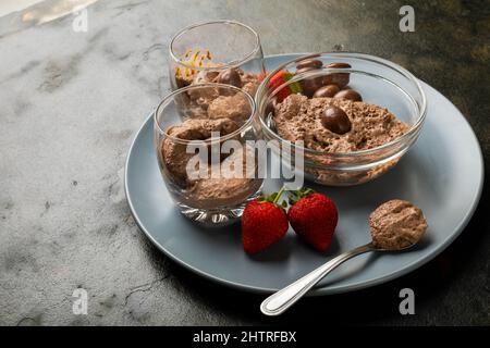 Primo piano di mousse al cioccolato con noci rivestite e fragole servite in ciotola e bicchieri sul piatto Foto Stock