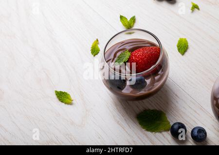 Primo piano fragola, mirtilli e foglia di menta con dessert al cioccolato servito in ciotola sul tavolo Foto Stock