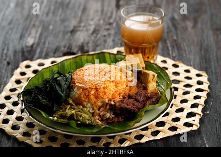 Il Nasi Padang o 'Padang Rice' è un famoso cibo tradizionale indonesiano. Riso con Rendang di manzo, foglie di manioca e pasta di peperoncino verde. Su tavoletta di legno Foto Stock