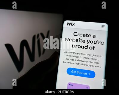 Persona che detiene il cellulare con il sito web della compagnia software israeliana Wix.com Ltd. Sullo schermo di fronte al logo. Concentrarsi sul centro del display del telefono. Foto Stock