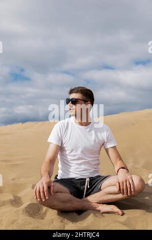 L'uomo in occhiali da sole seduti in loto posa in deserto sulla sabbia Foto Stock
