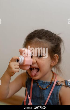 bambina unny che fa la foto con la macchina fotografica giocattolo rosa, mostrando la lingua Foto Stock