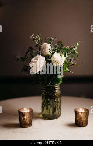 Bouquet di rosa bianca in un vaso, e candele d'oro, in una luce drammatica Foto Stock