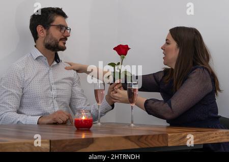 Coppia caucasica che ha un appuntamento romantico con bicchieri di champagne rosa, rosa rossa, e una candela Foto Stock