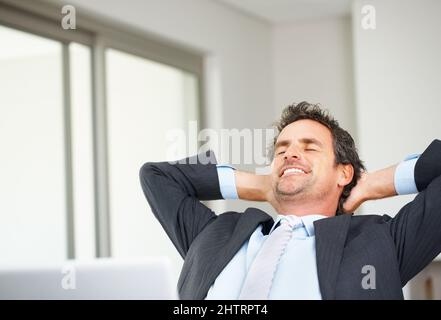 Un dirigente rilassato con un notebook. Uomo d'affari maturo e intelligente che utilizza un notebook e si rilassa con le mani dietro la testa. Foto Stock