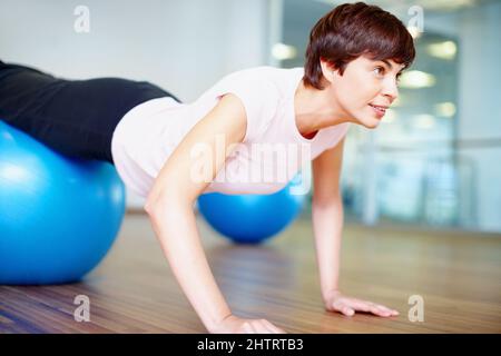 Spingere verso l'alto. Donna che fa push up utilizzando pilates palla durante una sessione di allenamento. Foto Stock