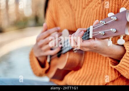 Primo piano della ragazza che suona l'ukulele in un giardino con chitarra acustica, fuoco selettivo delle mani della donna che suonano le corde dell'ukulele. Foto Stock