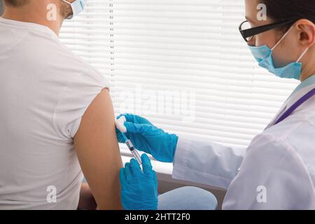 Il medico tiene una siringa prima di fare un'iniezione a un paziente in una maschera medica. Covid-19 o vaccino contro il coronavirus. Vaccinazione della popolazione Foto Stock