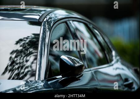 Vista laterale del moderno e pulito verde oliva parcheggio auto su una strada dopo la pioggia, gocce di pioggia sulla superficie della macchina. Foto Stock