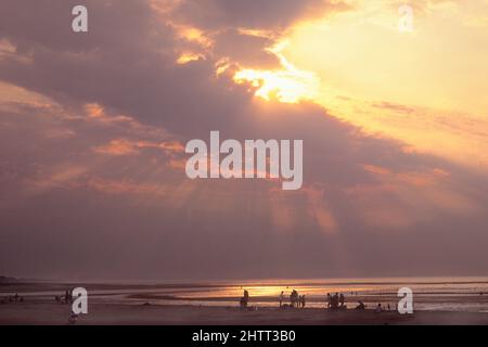 Sunbeams sopra Cabourg, costa della Normandia,.Tramonto sopra l'Oceano Atlantico. Sole dietro le nuvole scure. Silhouette di persone sulla spiaggia. Cote Fleurie, Francia Foto Stock