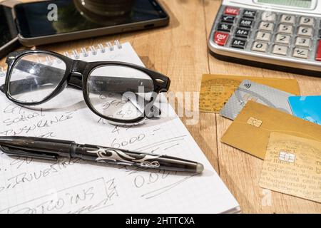Una scrivania con un blocco note, penna, occhiali, calcolatrice e diverse carte di credito. Scrivania. Finanza personale. Metodi di pagamento. Foto Stock