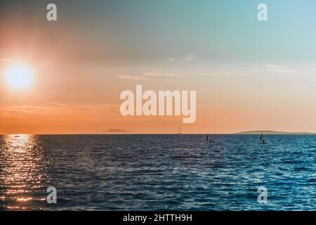 Tramonto, mare blu e quattro persone su due tavole sup sul mare. Un bellissimo tramonto dai colori blu e arancio del cielo. Foto Stock