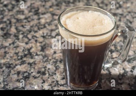 caffè tonico in una tazza trasparente che si trova su un tavolo marmore, clima urbano sullo sfondo. Foto Stock